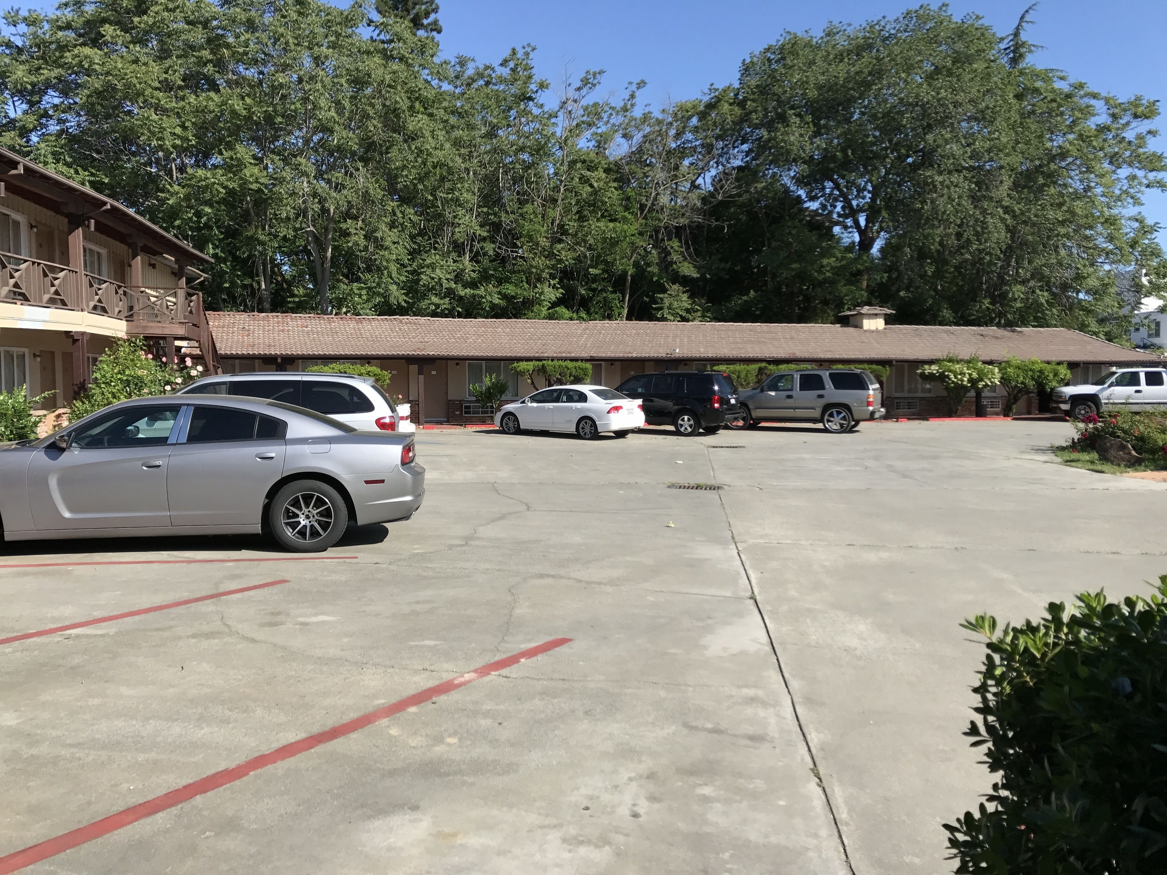 A parking lot with several cars, a building with a tiled roof, and trees in the background.