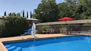 Una piscina con borde de azulejos azules, un puesto de salvavidas y un paraguas rojo.