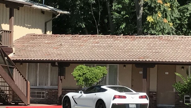Un coche deportivo blanco estacionado frente a un edificio con techo de tejas y una escalera.