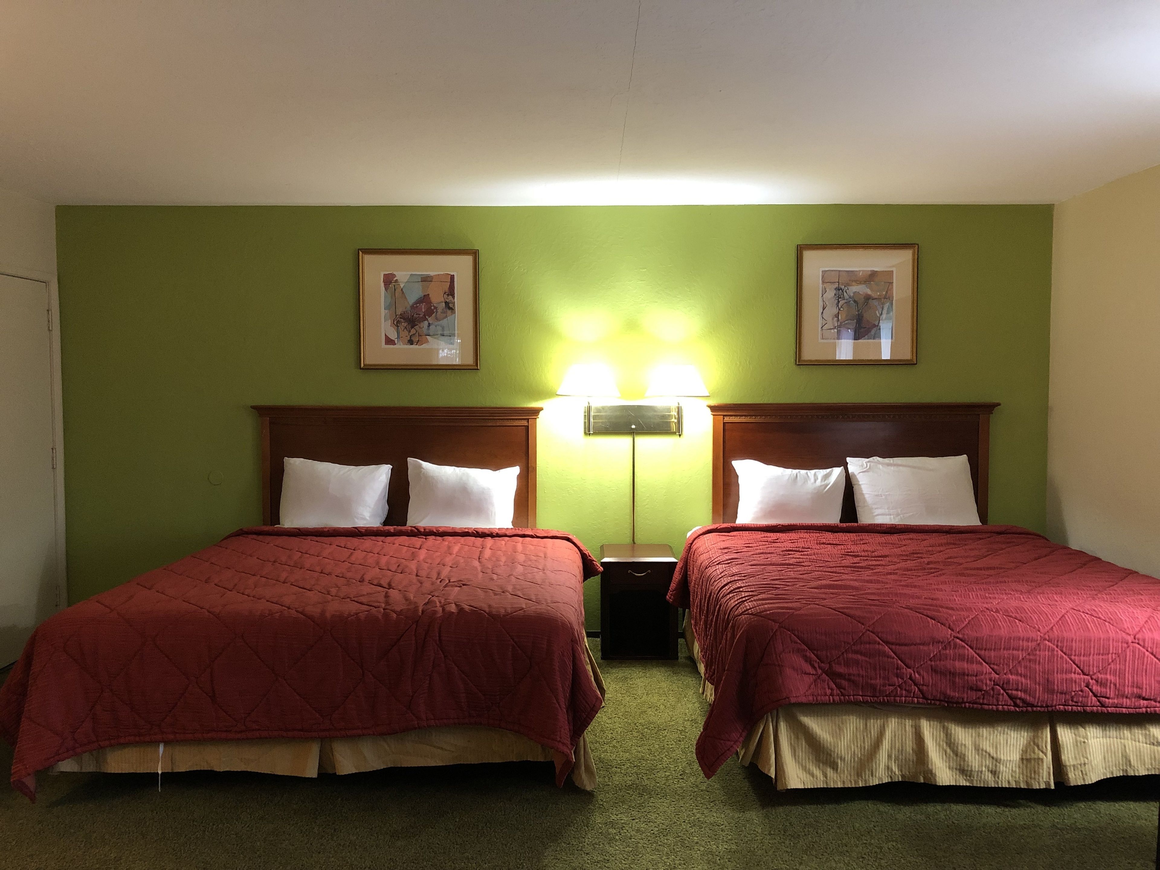 A hotel room with two beds, green walls, and framed artwork above each bed.