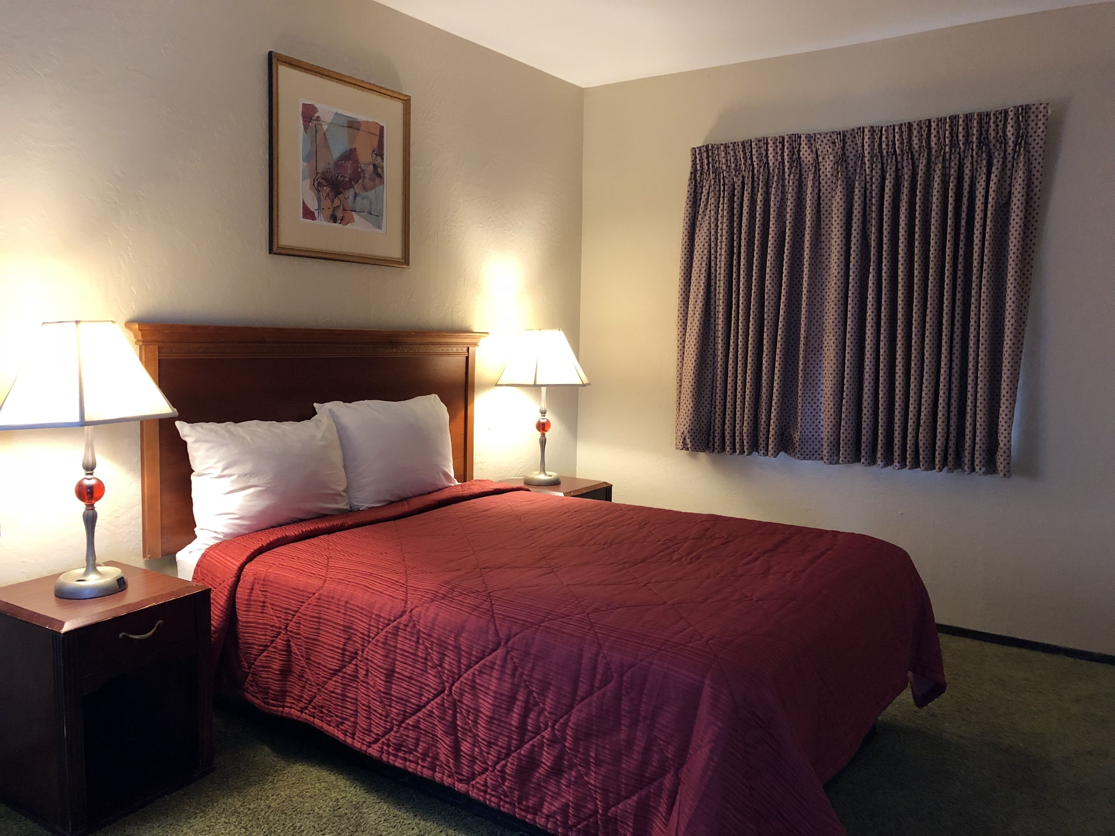 A hotel room with a large bed, two bedside tables with lamps, a framed picture on the wall, and a window with curtains.