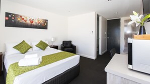A hotel room with a bed, a desk, a chair, a painting on the wall, and a door leading to another room. - Icon on Isa (Mount Isa City)