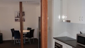 A modern kitchen with white cabinets, a built-in oven, and a microwave. There is a dining area with a table and chairs. - Icon on Isa (Mount Isa City)