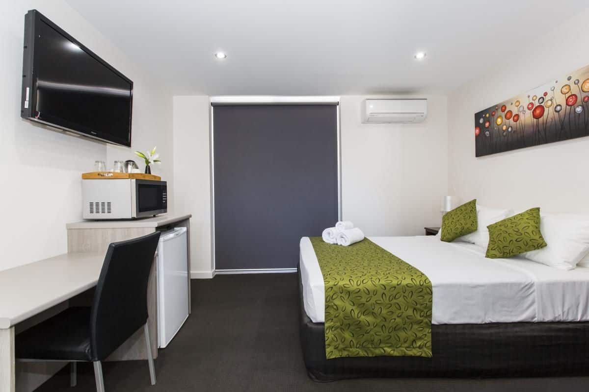 Quarto de hotel com cama, escrivaninha com micro-ondas, televisão e um quadro na parede.