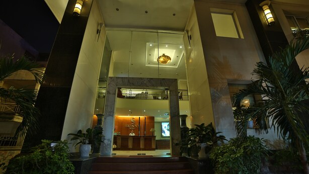 Entrada de hotel con mostrador de recepción, una escalera que sube y plantas en macetas.