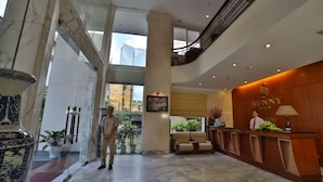 Un vestíbulo de hotel con una recepción, un jarrón grande y una escalera.