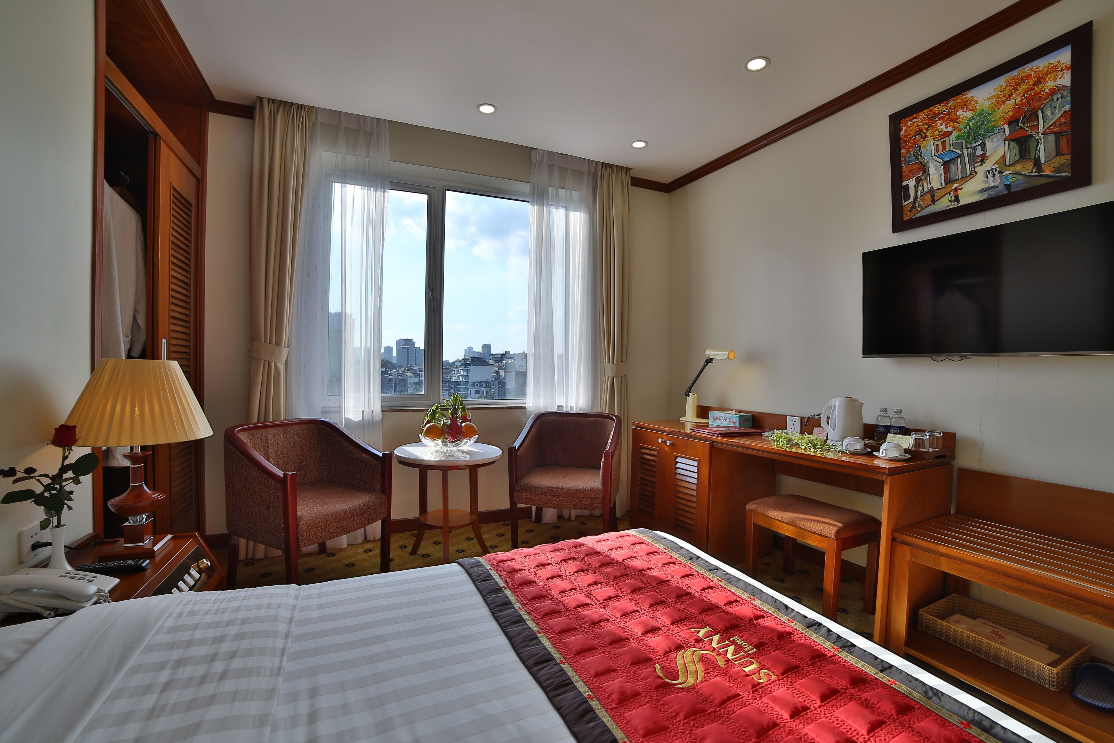 Una habitación de hotel con una cama grande, un escritorio con una silla, una mesita con una planta y un televisor montado en la pared.
