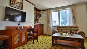 Habitación de hotel con televisor de pantalla plana, escritorio de madera, sofá y mesa de comedor con fruta.