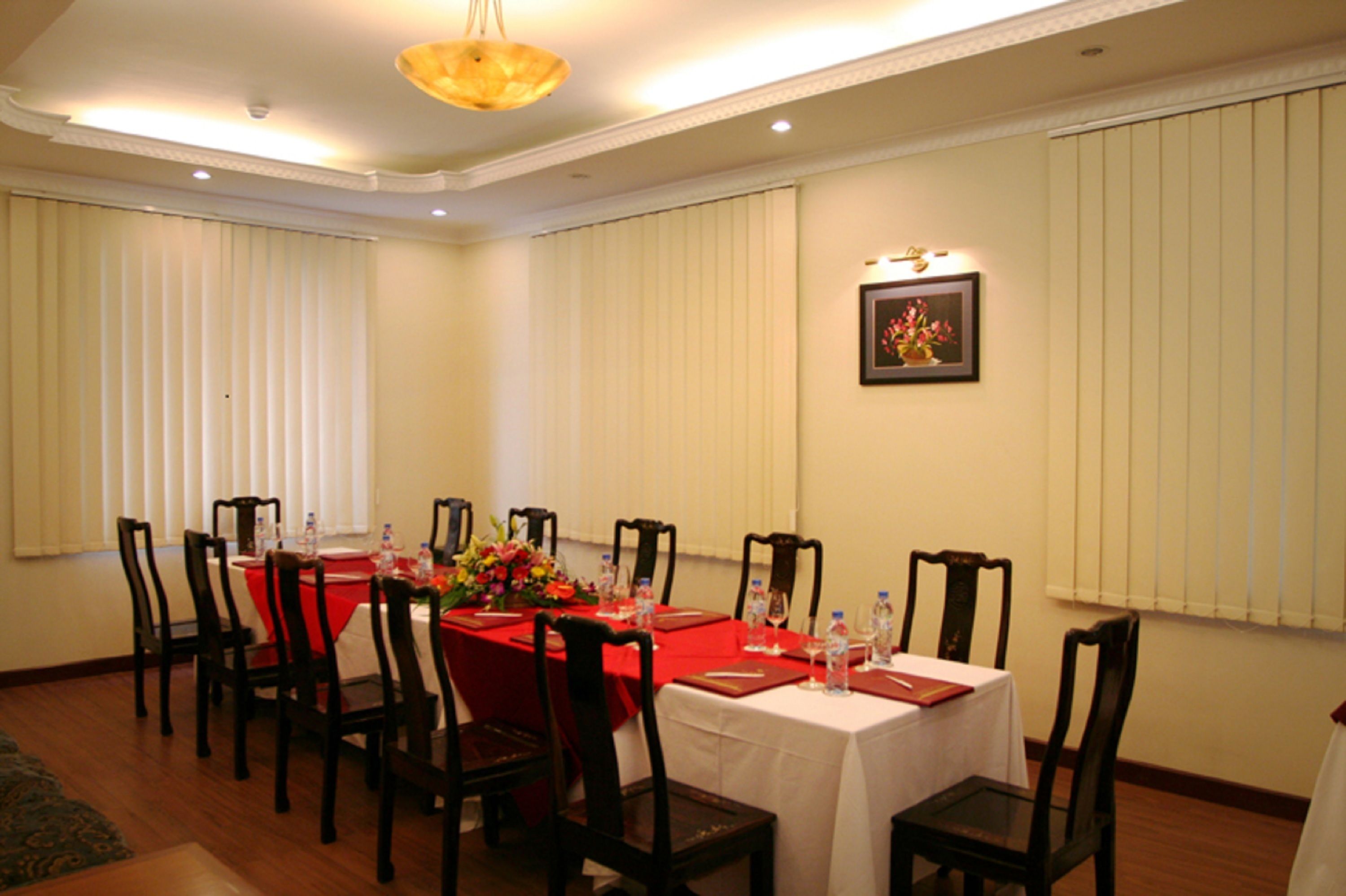 Une salle à manger avec une table recouverte d’une nappe rouge, d’une nappe blanche et des chaises en bois. Un tableau encadré est accroché au mur.