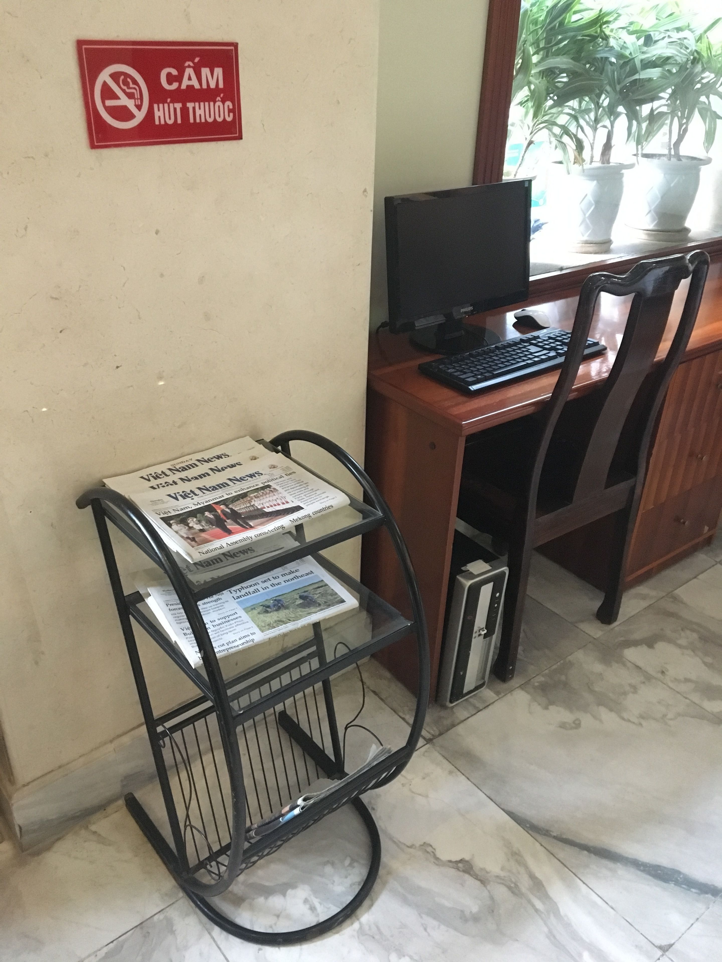A desk with a computer, a chair, and a metal rack holding newspapers.