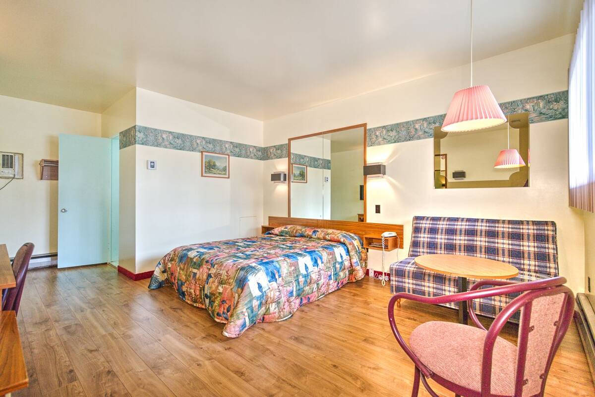 Un dormitorio con cama, una silla, una mesita, un espejo y una puerta.