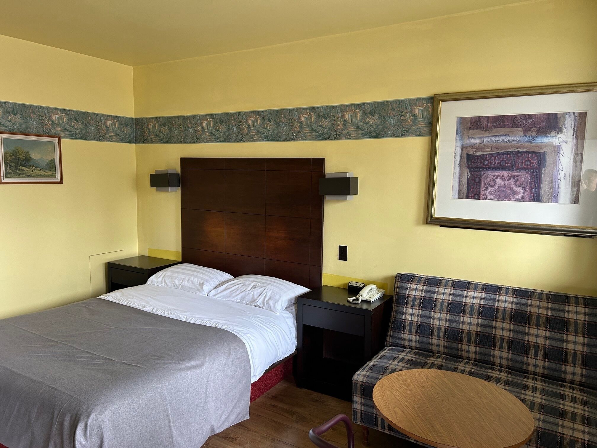 A hotel room with a bed, a bedside table with a phone, a chair, and a round table.