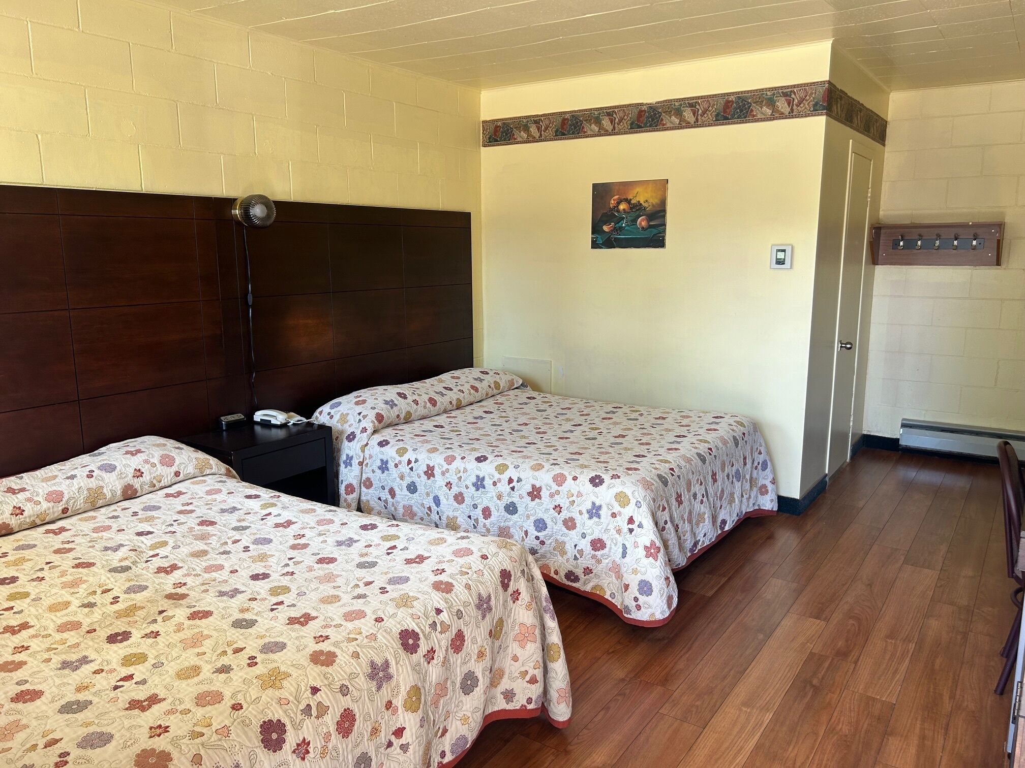 Una habitación con dos camas, cabecero de madera, una mesita de noche con un teléfono y un adorno en la pared.