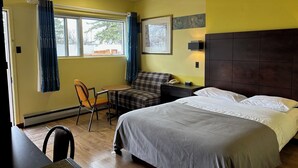 A hotel room with a bed, a desk, a chair, a sofa, and a window with curtains. - Motel R-100 (Longueuil)