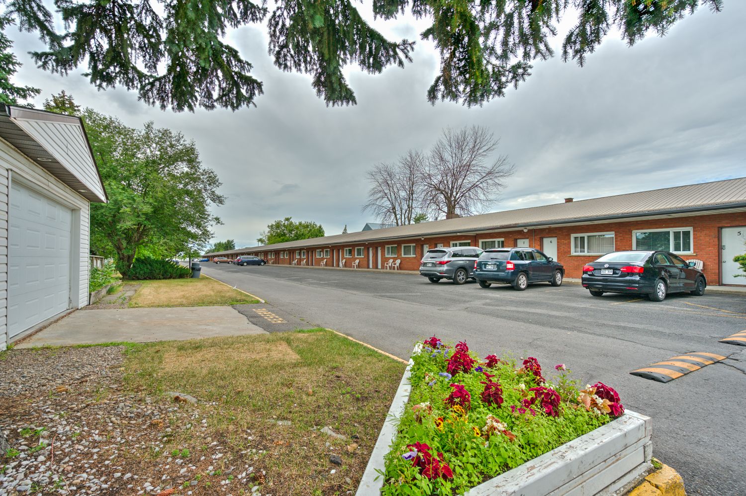 Ein Motel mit einer Reihe von Zimmern, einem Parkplatz und einem Blumenbeet im Vordergrund.