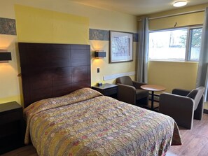 A hotel room with a bed, a desk, a chair, a small table, and a window with curtains.