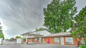 A single-story building with a 'Reception' sign, a covered parking area, and a brick facade. - Motel R-100 (Longueuil)