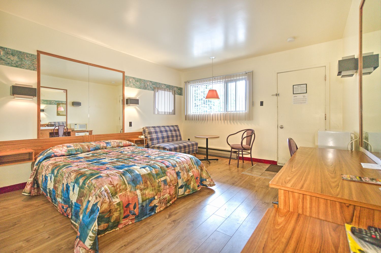 Ein Hotelzimmer mit einem großen Bett, einem Holztisch, einem Stuhl, einem kleinen Tisch und einem Spiegel.