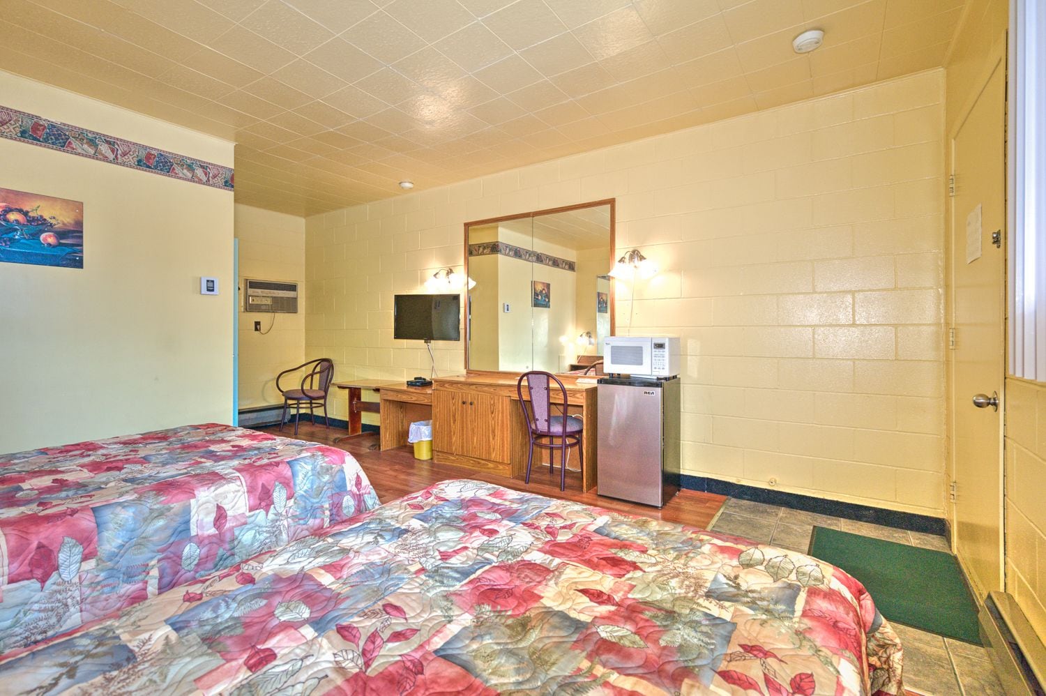 Une chambre de motel avec deux lits, un bureau, une chaise, un réfrigérateur et un grand miroir.