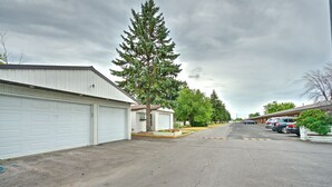 A street view of a residential area with single-story houses, a large evergreen tree, and a row of parked cars. - Motel R-100 (Longueuil)