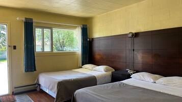 Una habitación con dos camas, piso de madera, pared de ladrillo y una ventana con cortinas.