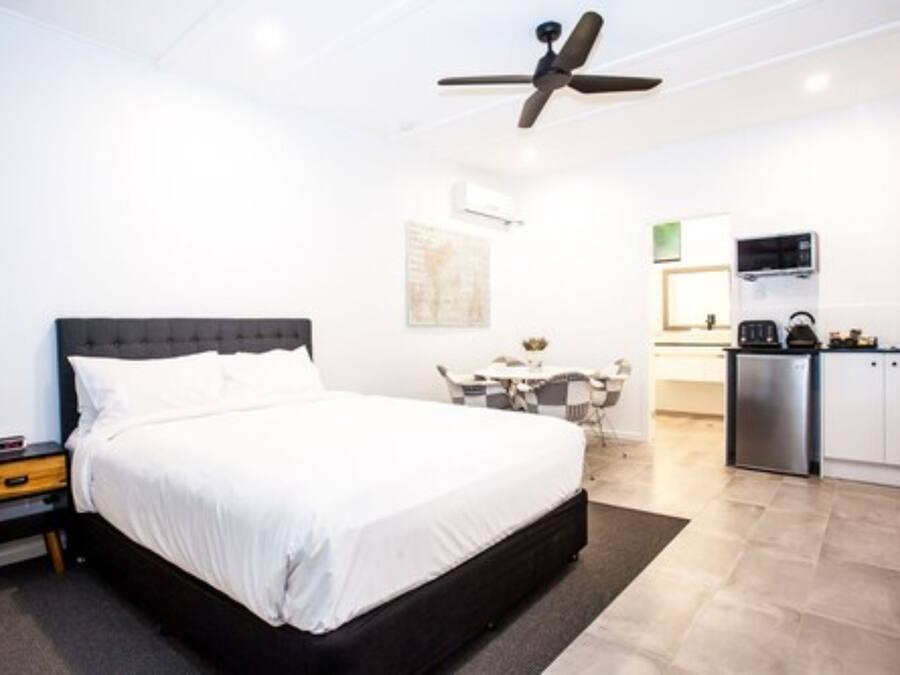 A modern hotel room with a large bed, a desk, and a kitchenette.