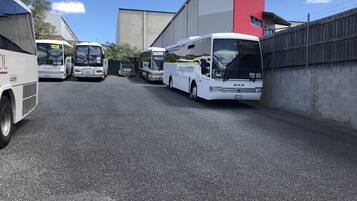 A row of buses parked in a lot with a building in the background.