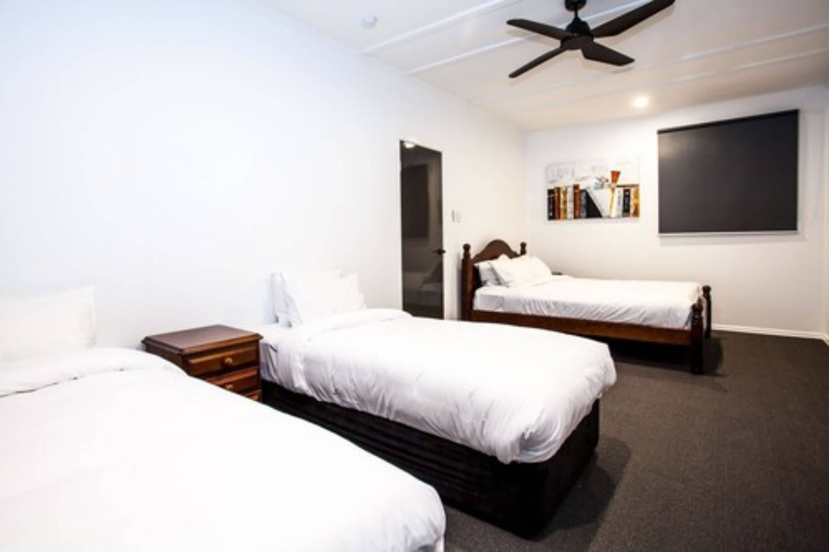 A hotel room with two single beds, a wooden nightstand, a ceiling fan, a bookshelf, and a large window.