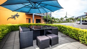 An outdoor seating area with a table and chairs, a large blue umbrella, and a building with a yellow wall and a lizard decoration. - Darra Motel and Conference Centre (Darra)