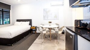A compact hotel room with a bed, a dining table with chairs, a small kitchen area, and a ceiling fan. - Darra Motel and Conference Centre (Darra)