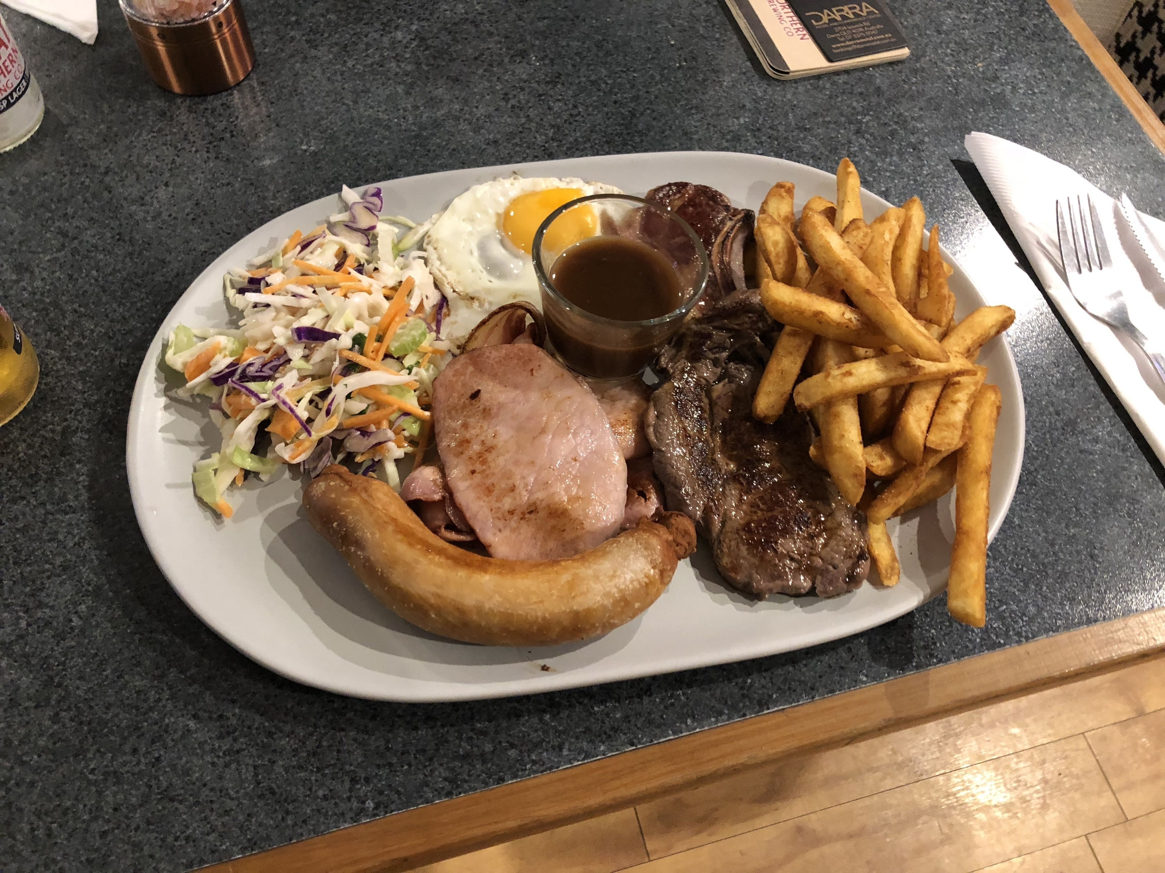 A plate with a variety of food including a steak, fries, a fried egg, and a coleslaw salad.