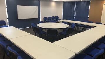 A conference room with a large oval table, blue chairs, and a projector screen.