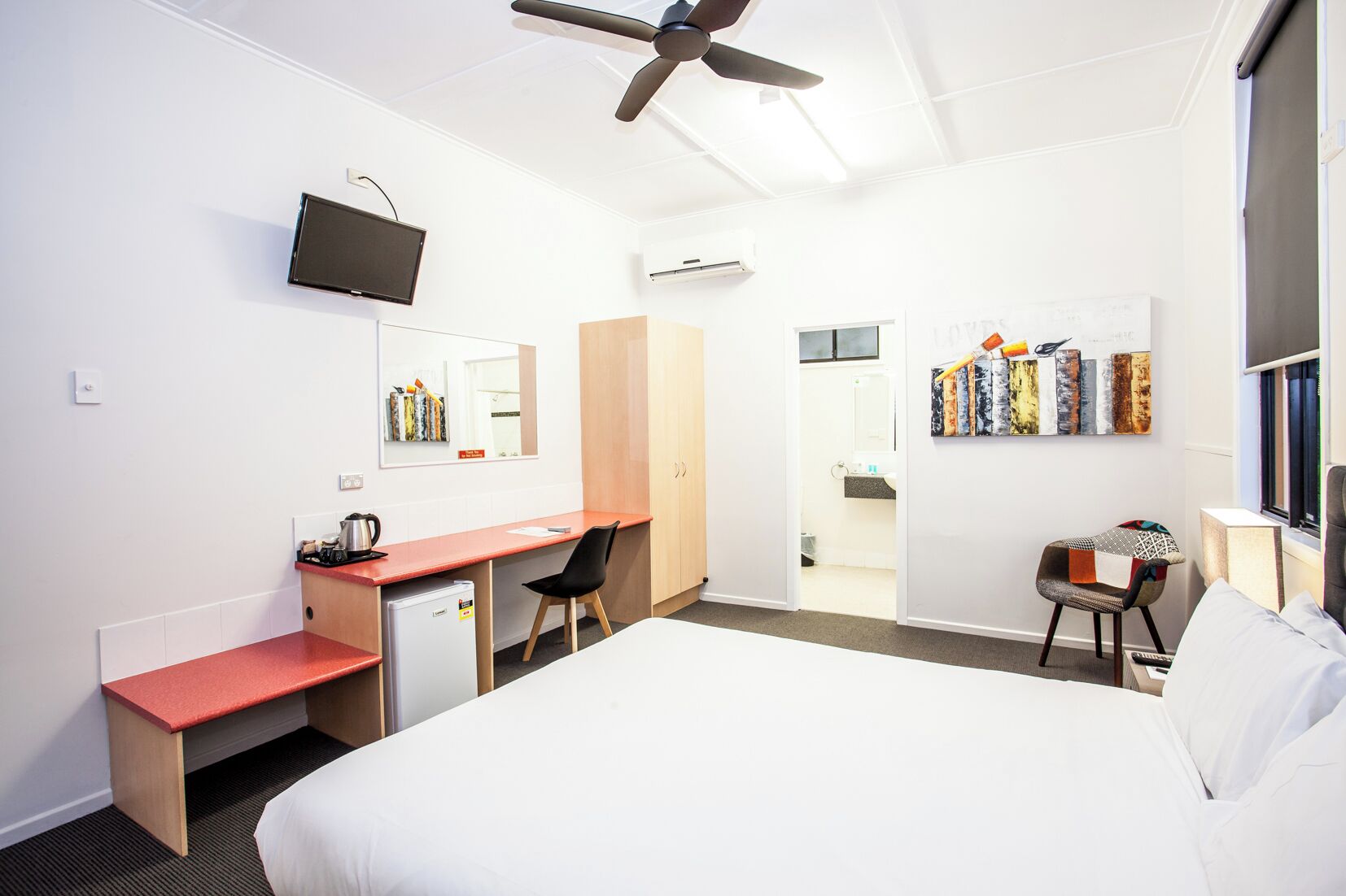 A hotel room with a bed, a desk, a chair, a television, and a ceiling fan.