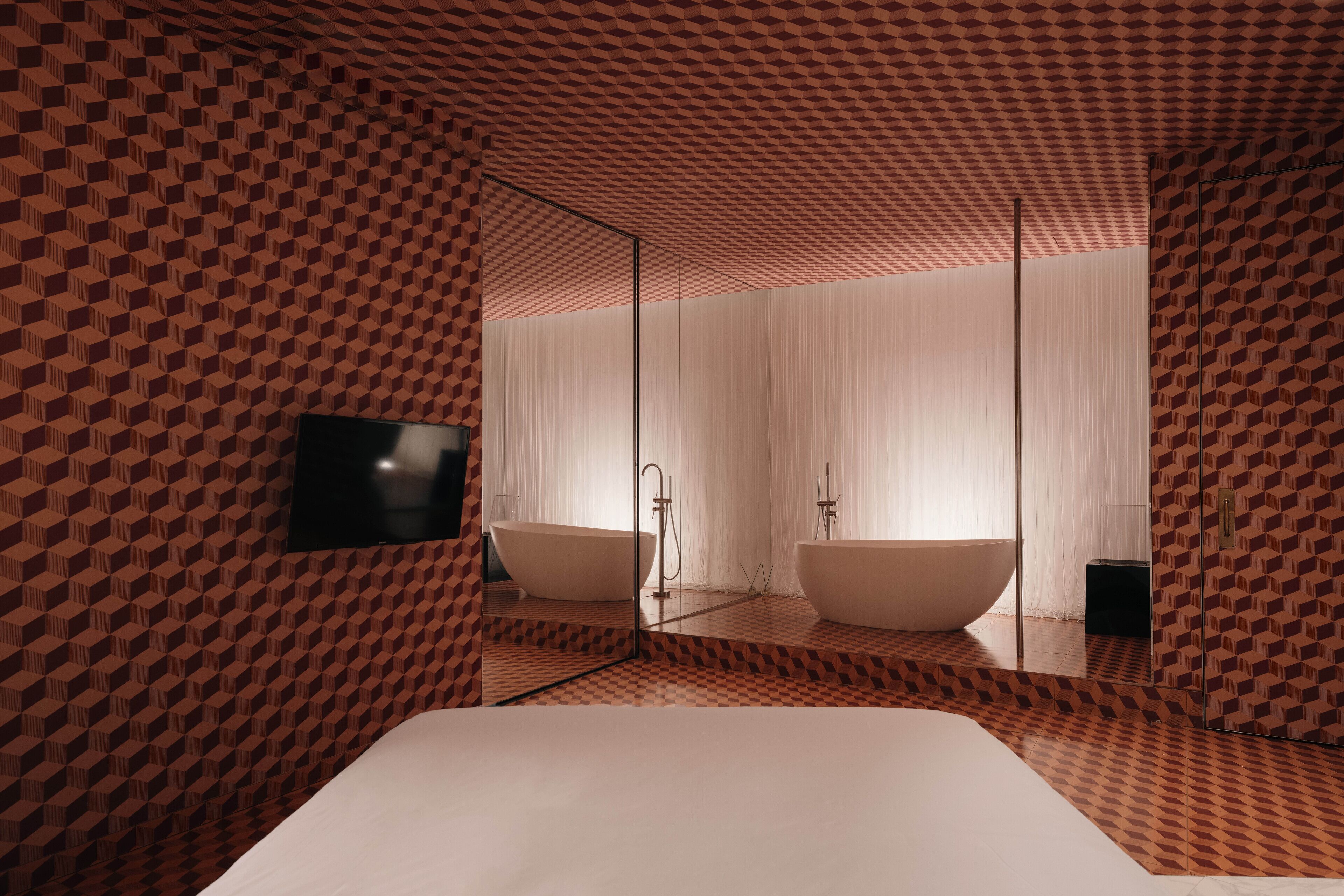 A modern bathroom with a large bathtub, a mirror, and a television mounted on the wall.