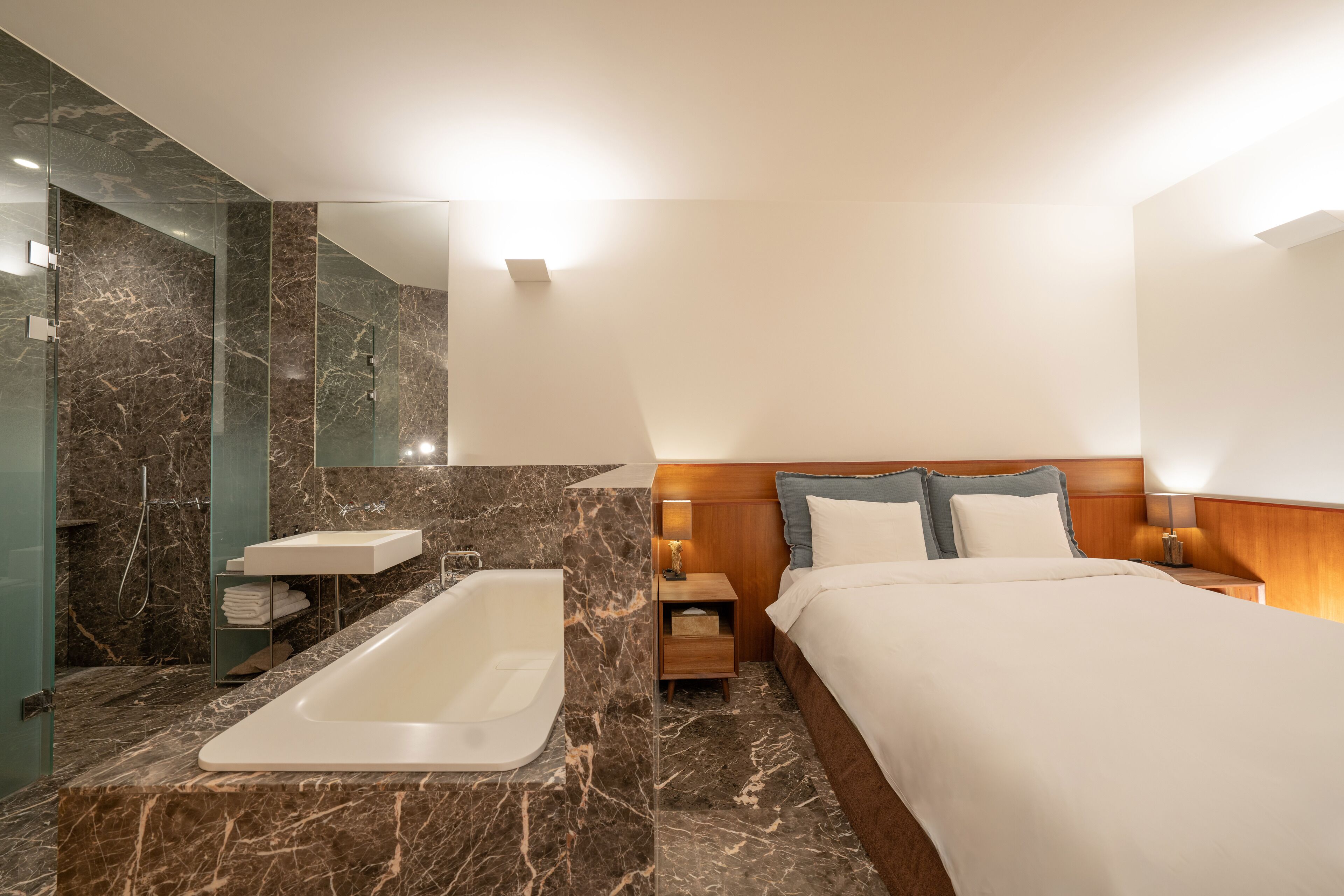 A modern hotel room with a marble bathroom, a large bed, and a wooden headboard.