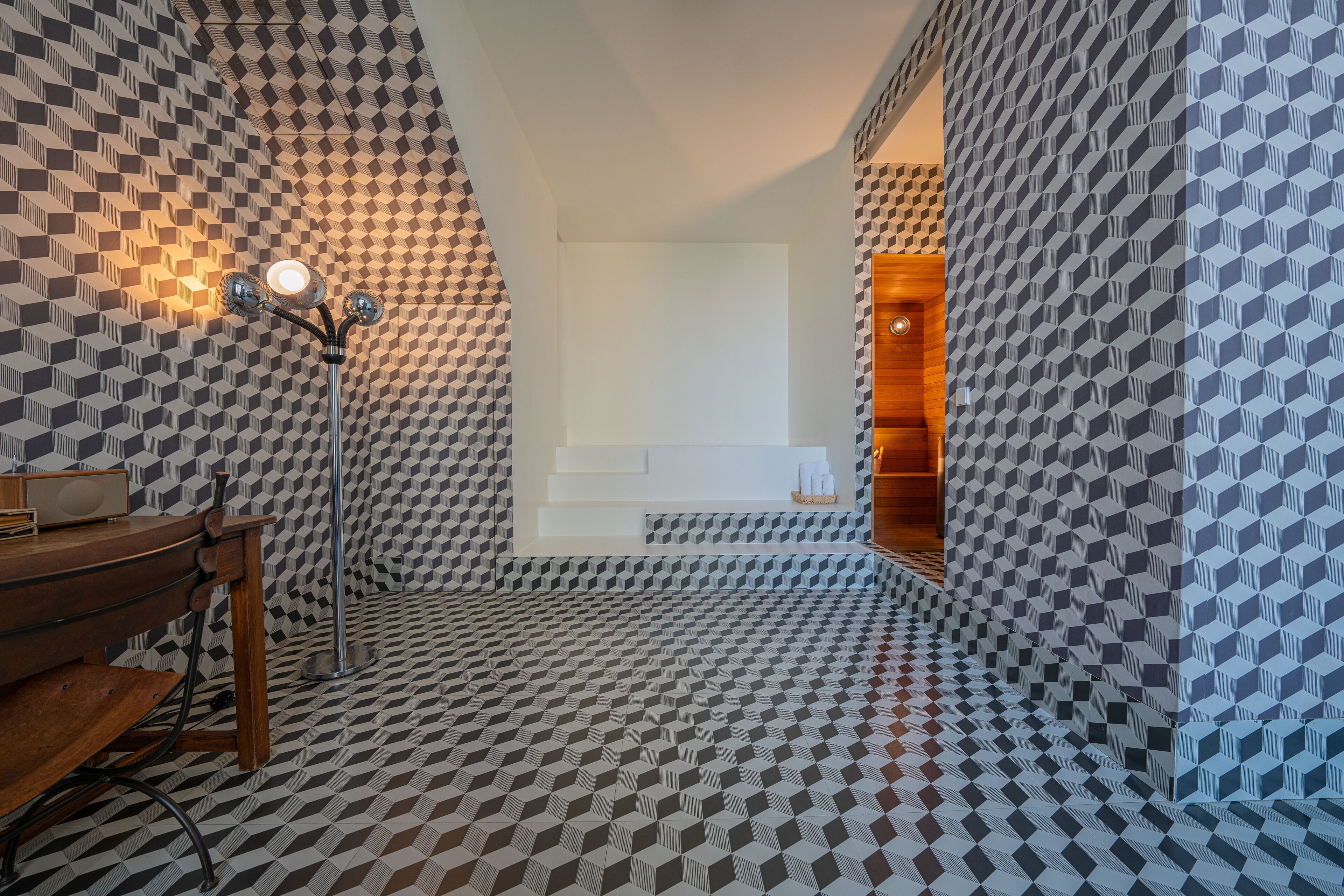 A bathroom with a geometric patterned floor and walls, a wooden vanity, and a mirror with a light fixture.
