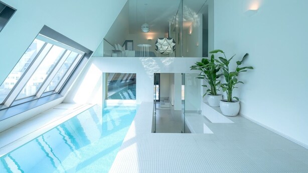 Una piscina interior moderna con paredes de vidrio, un entrepiso y plantas en macetas.