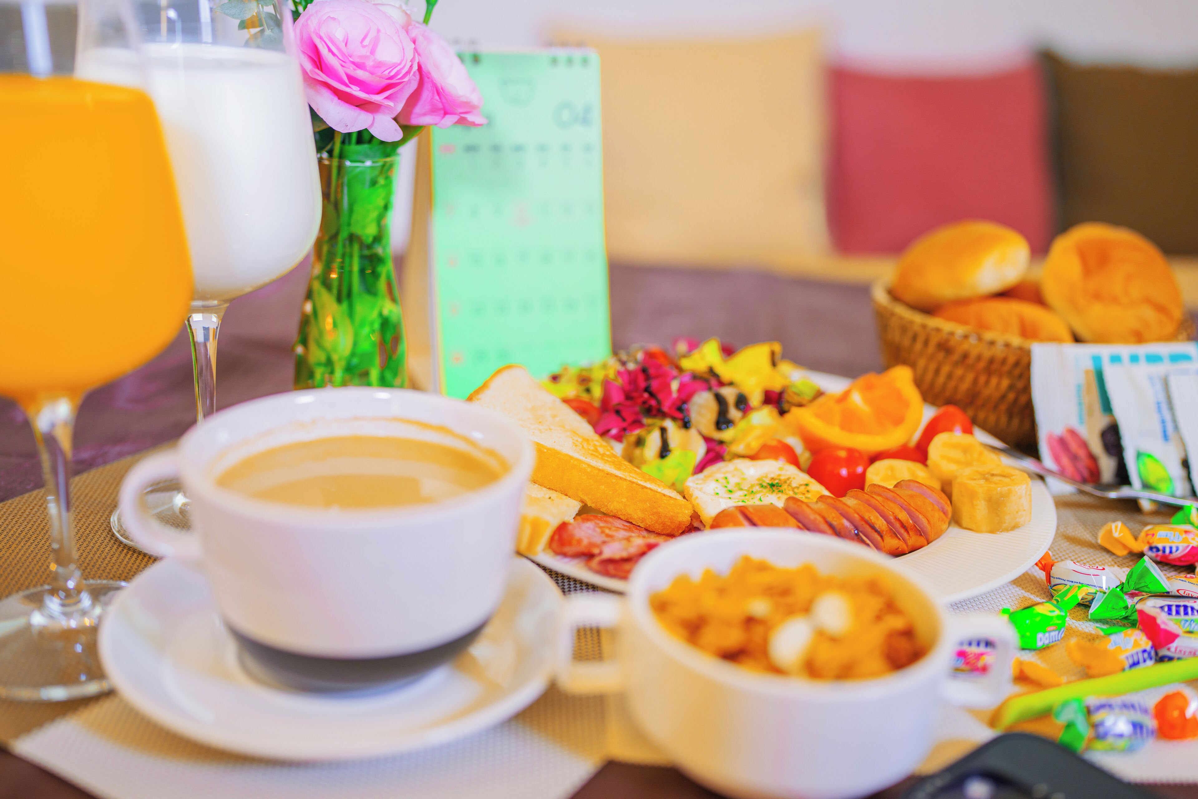 Una mesa de desayuno con una taza de café, un vaso de jugo de naranja, un plato de pasteles y una cesta de panecillos.