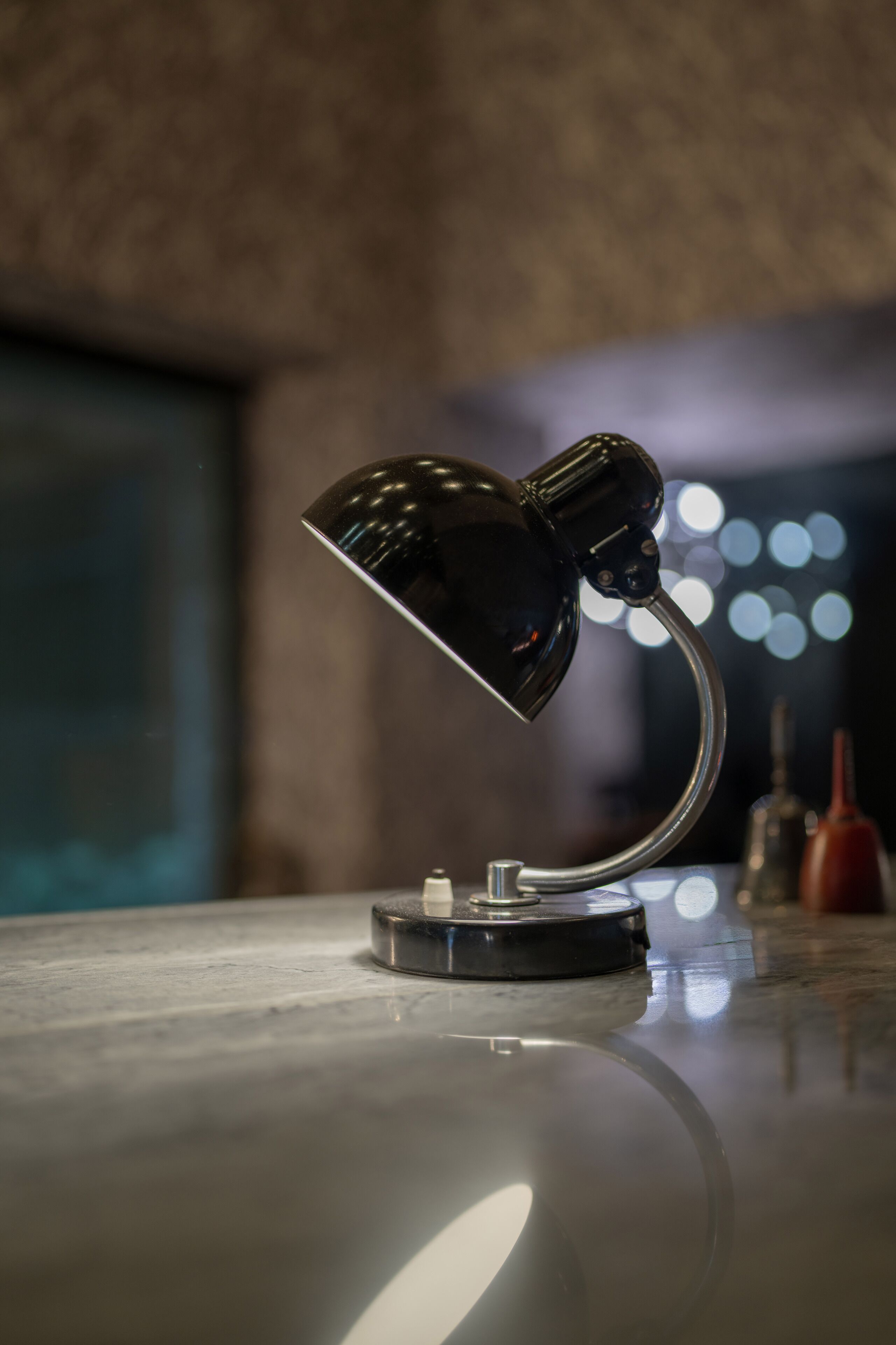 A desk lamp with a metallic base and curved neck, positioned on a reflective surface.