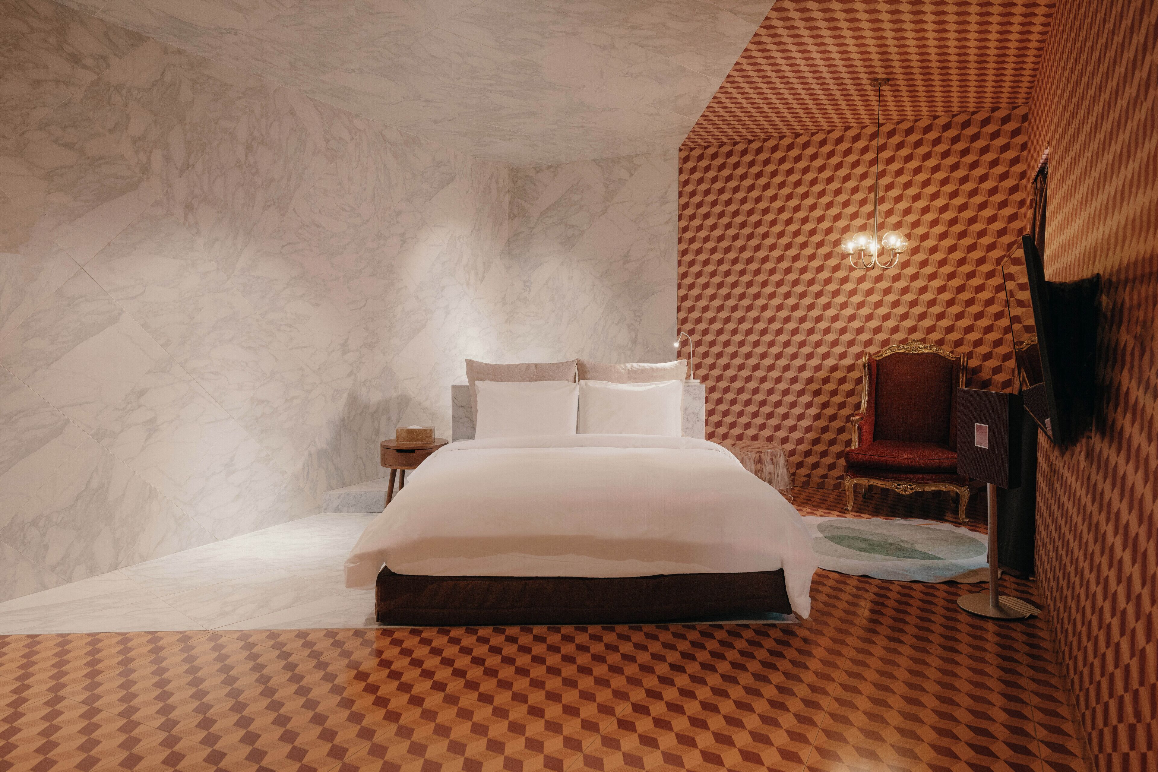Un dormitorio con una cama grande, una mesita de noche, una silla y un papel tapiz estampado.