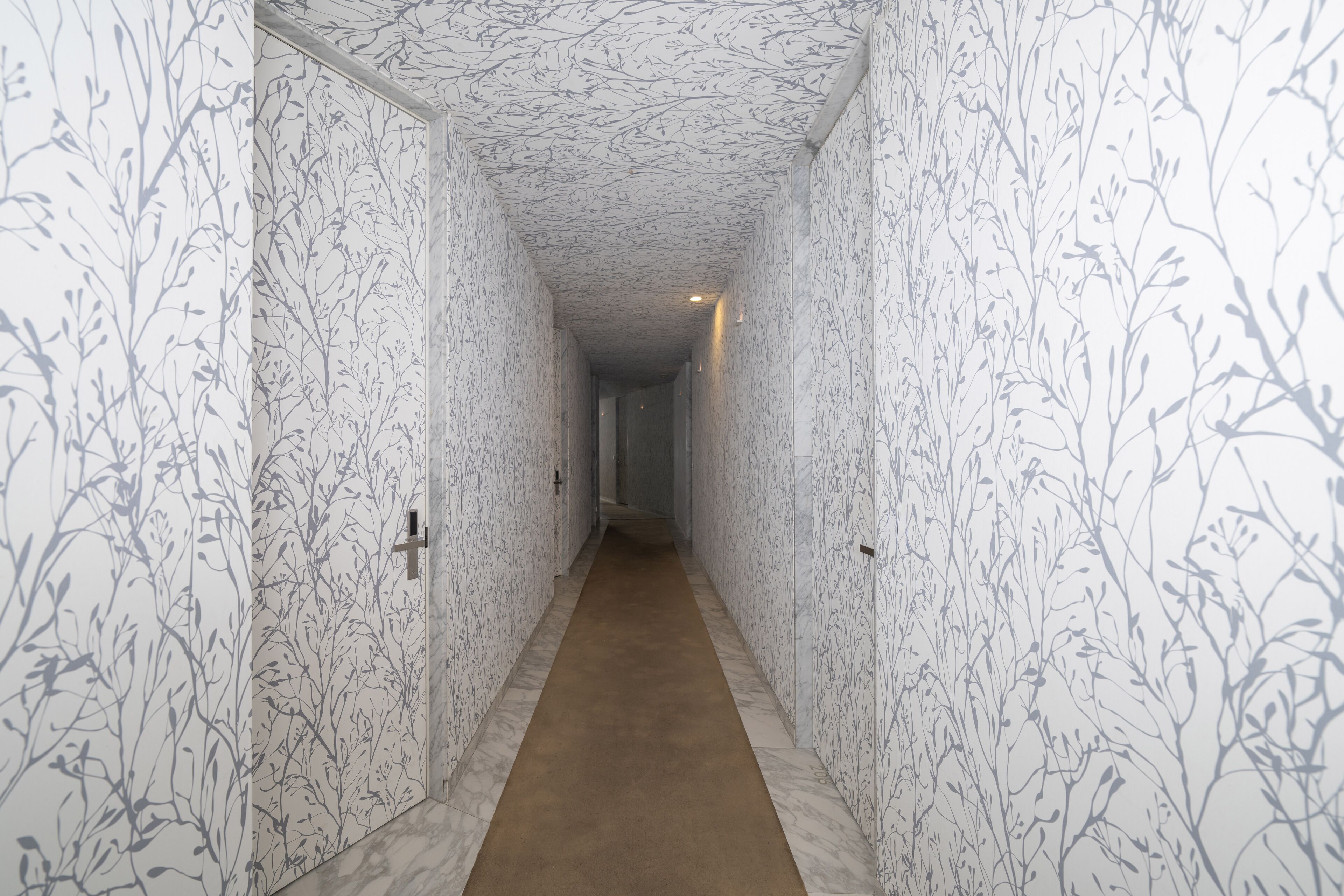 A hallway with patterned wallpaper and a marble floor.