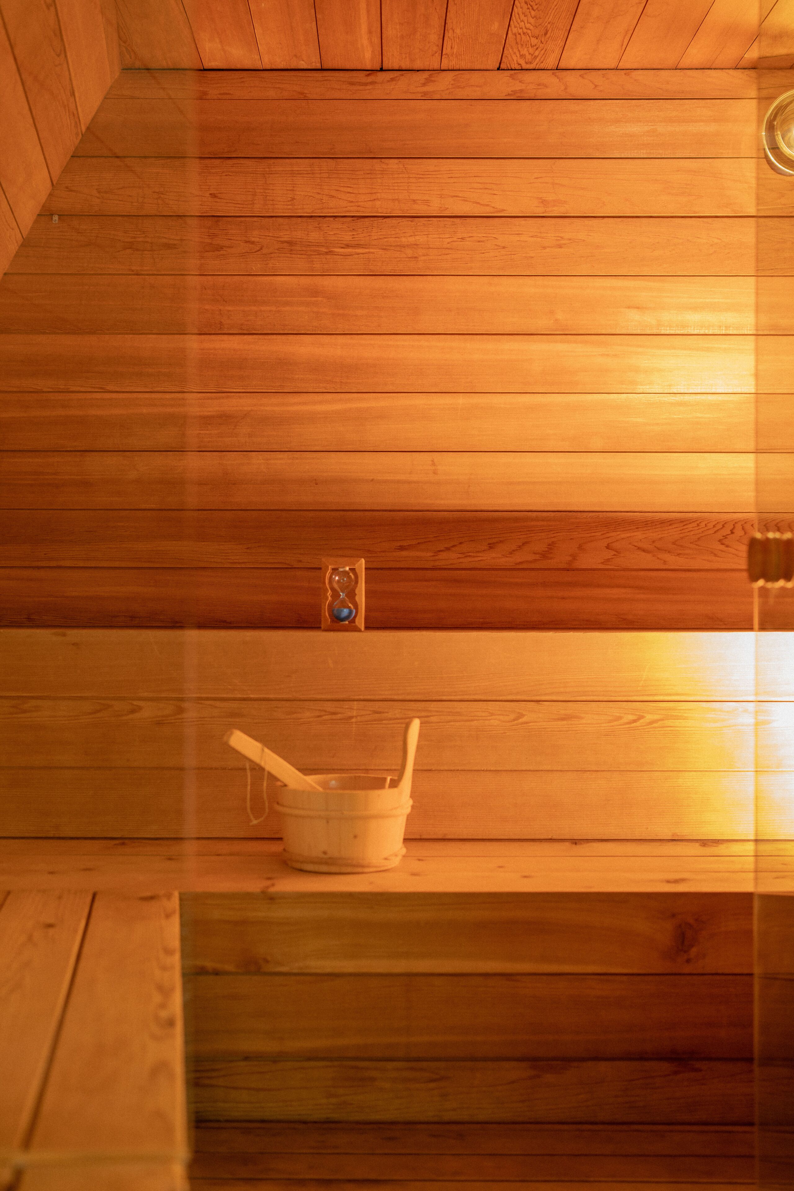 A wooden sauna with a wooden bench and a small hourglass on the wall.