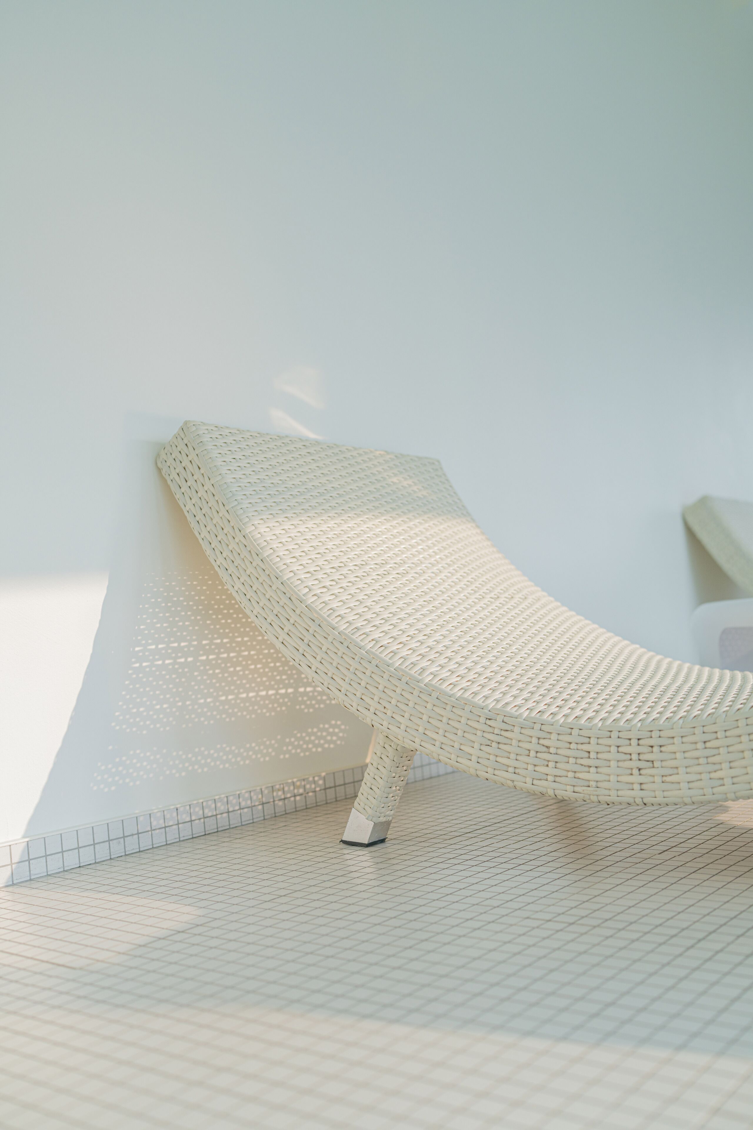 Une chaise en osier, placée devant un mur blanc, sur un sol à motifs géométriques.
