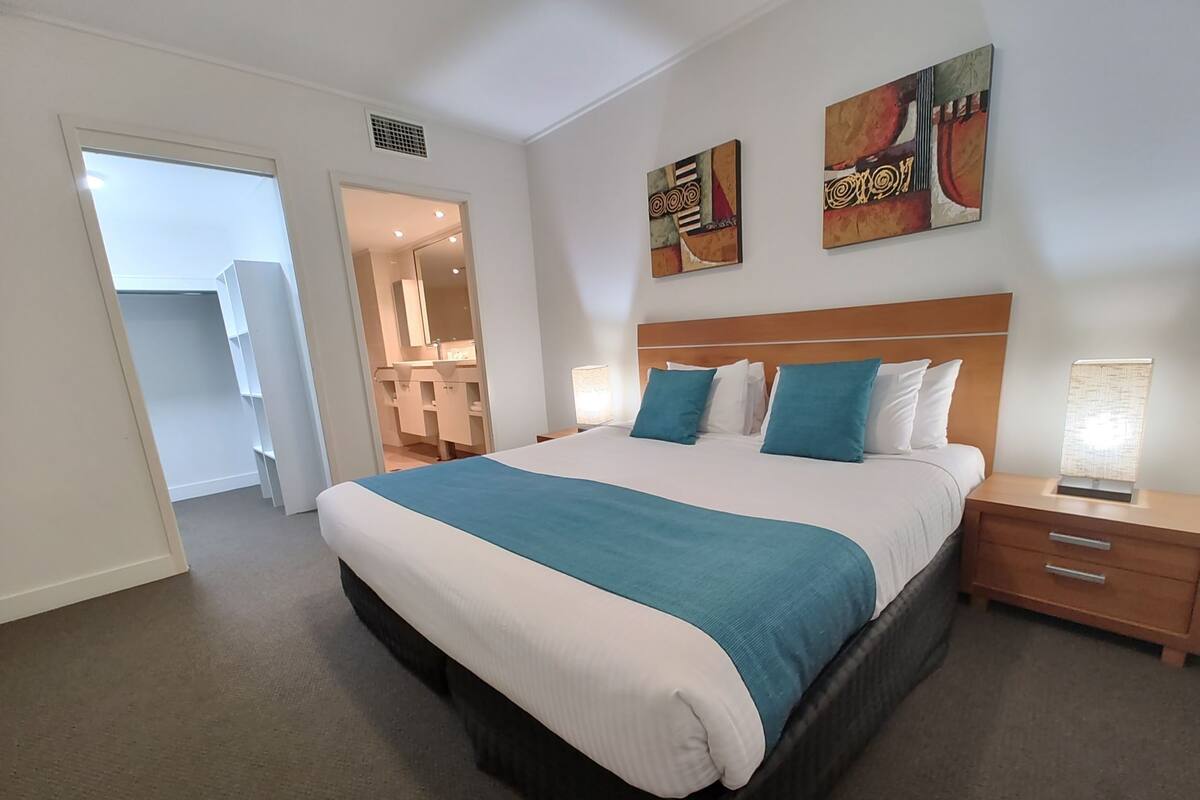 A hotel room with a large bed, a wooden headboard, two bedside tables with lamps, and artwork on the walls.