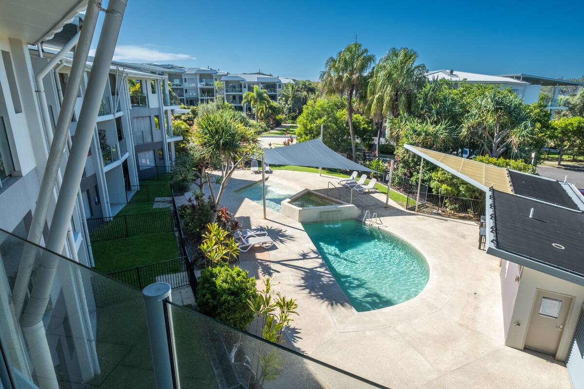 A hotel with a swimming pool, palm trees, and a covered area.
