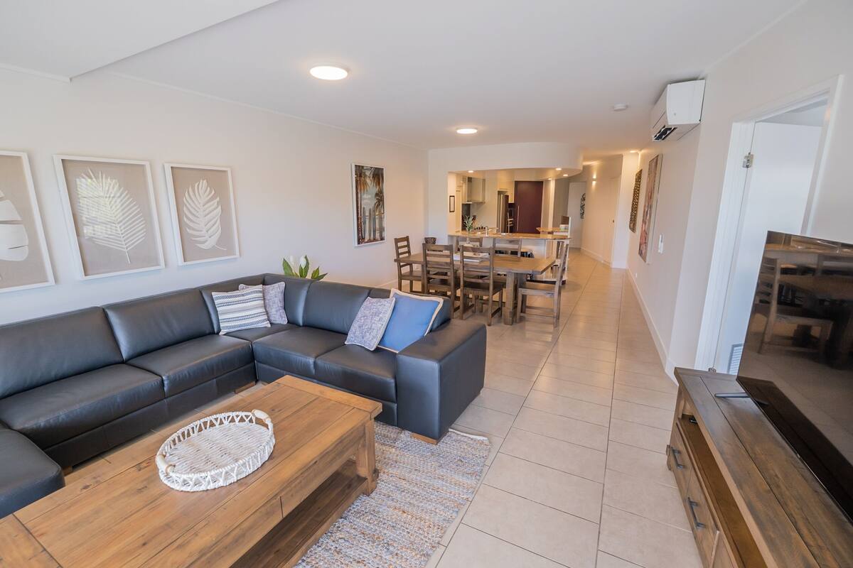 A modern living room with a sectional sofa, a wooden coffee table, and a dining area with a wooden table and chairs.