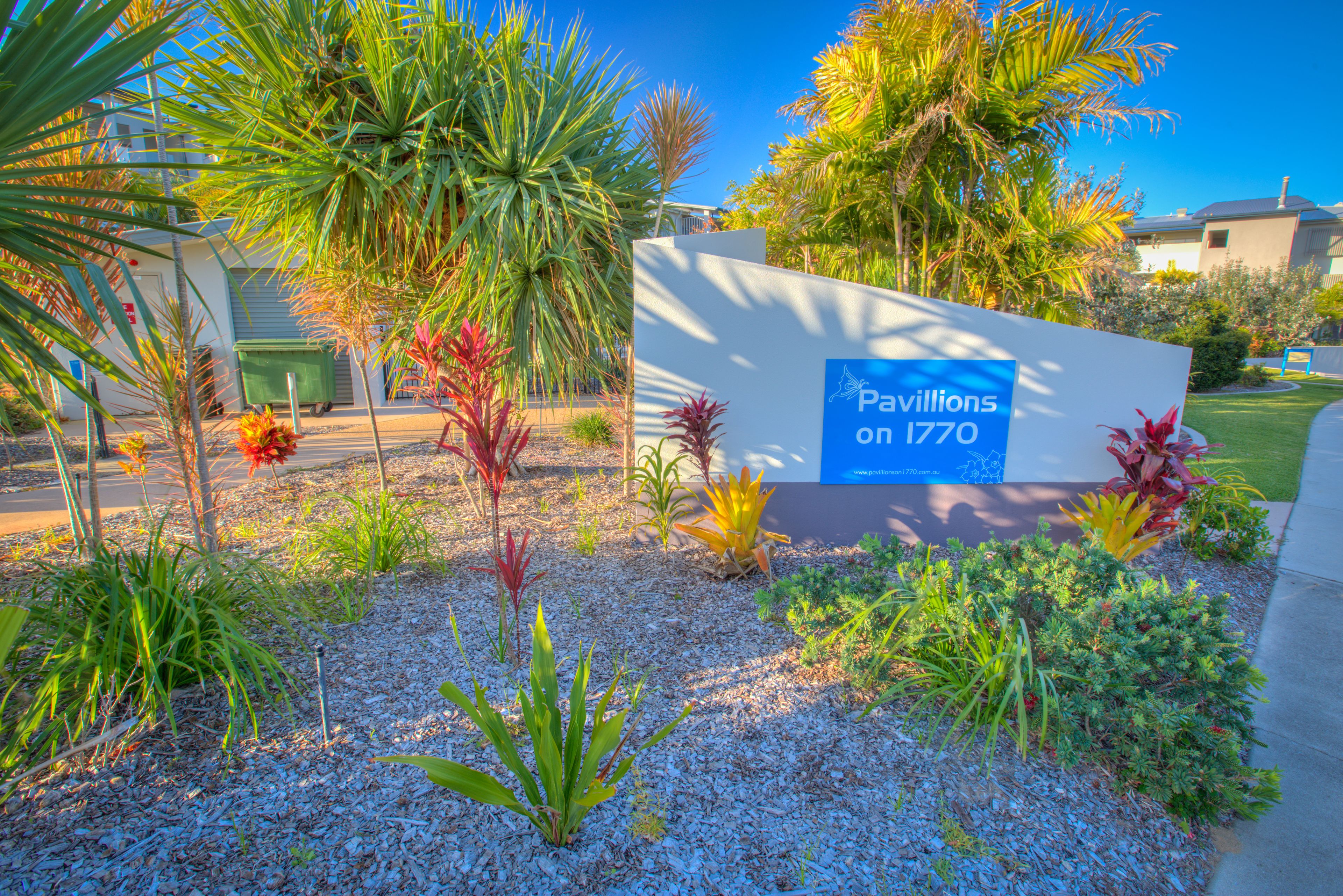 A sign for 'Pavilions on 1770' with a landscaped garden featuring various plants and a building in the background.