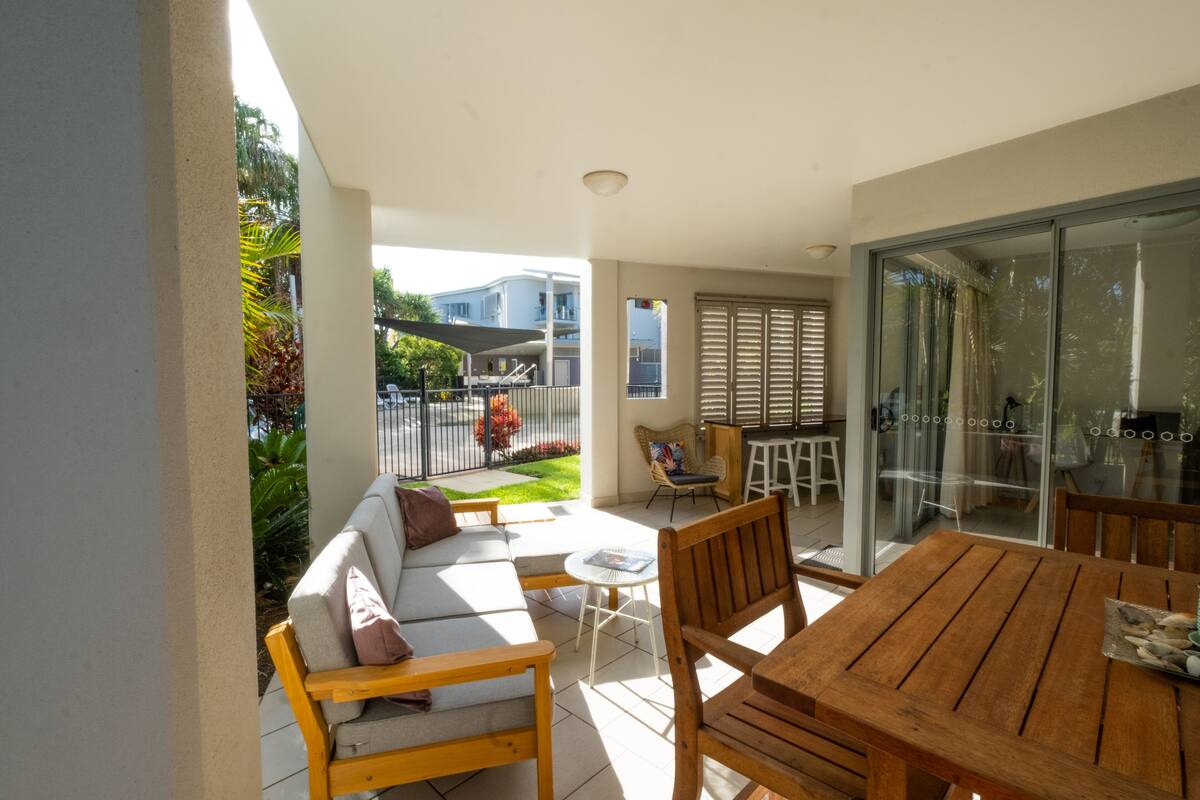A patio with a wooden table and chairs, a sofa, and a glass door leading to a balcony.