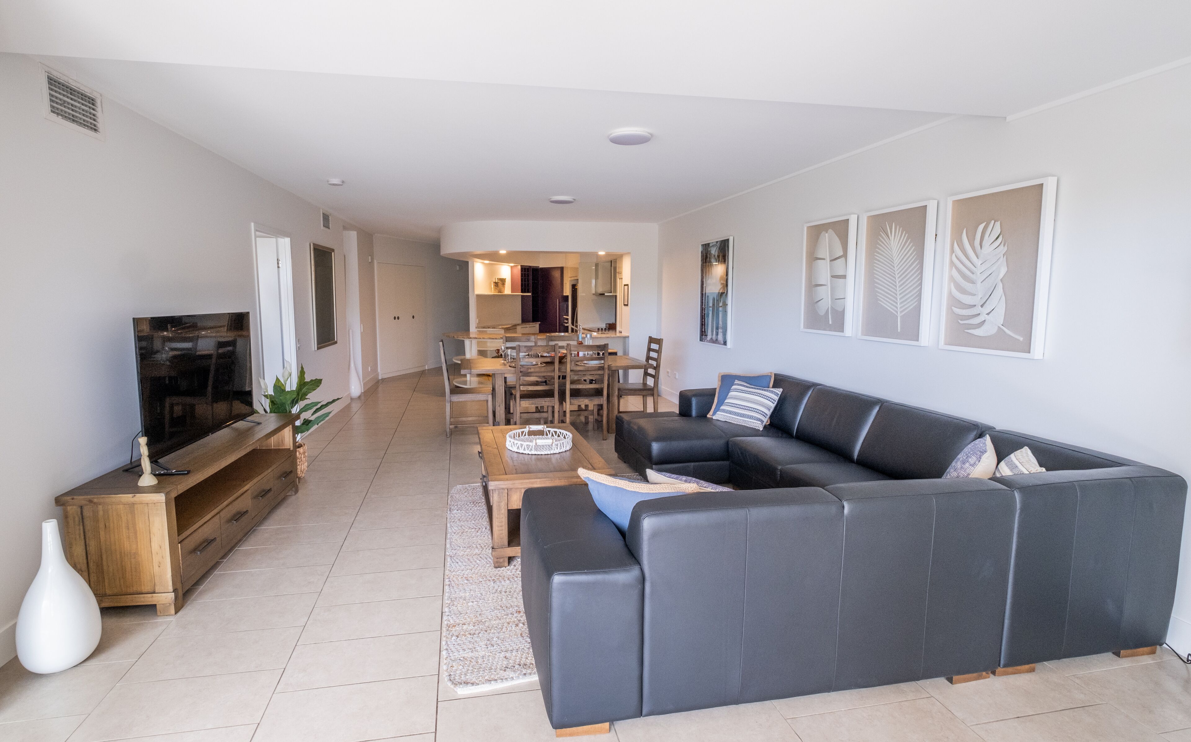 A modern living room with a dark leather sofa, wooden coffee table, and a flat-screen TV.