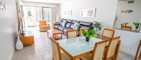 A dining area with a glass table and wooden chairs, a leather sofa, and a large mirror on the wall.